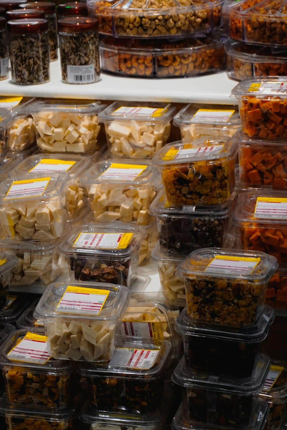 Frascos y recipientes transparentes con bocadillos variados sobre estantes blancos.